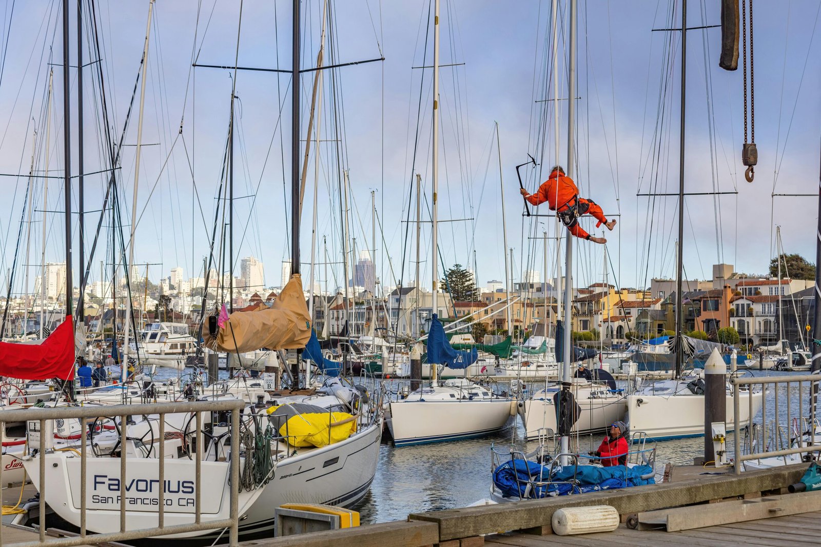 Workers fixing sailboats at a bustling San Francisco marina surrounded by a scenic cityscape.