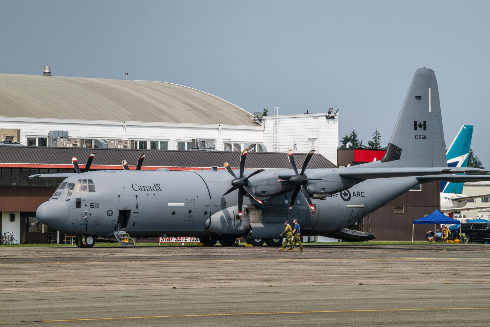 Canadian military transport aircraft on the runway at airport terminal with crew on ground.